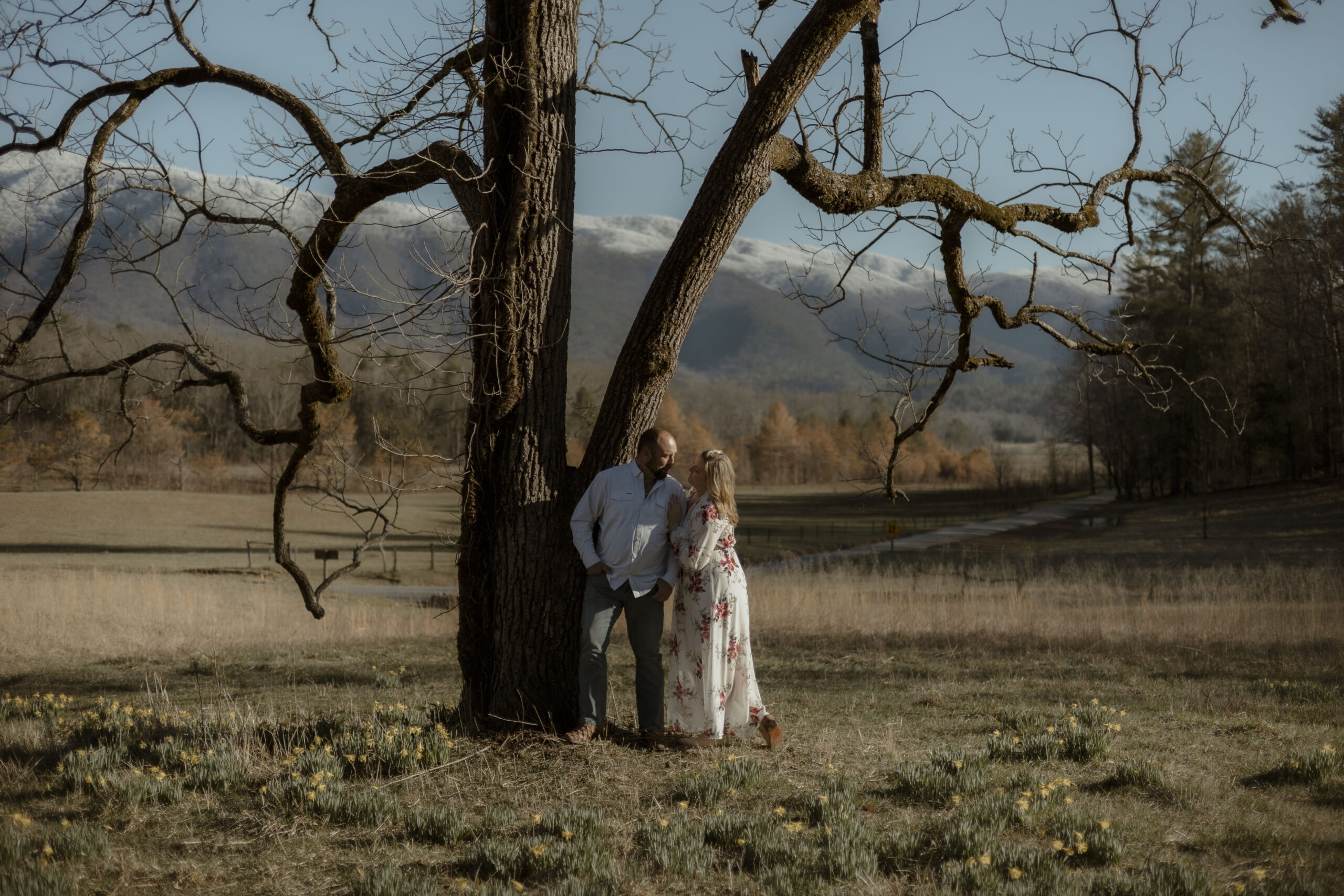 Couple stares into each others eyes while standing in a field of wildflowers in front of snow covered mountains