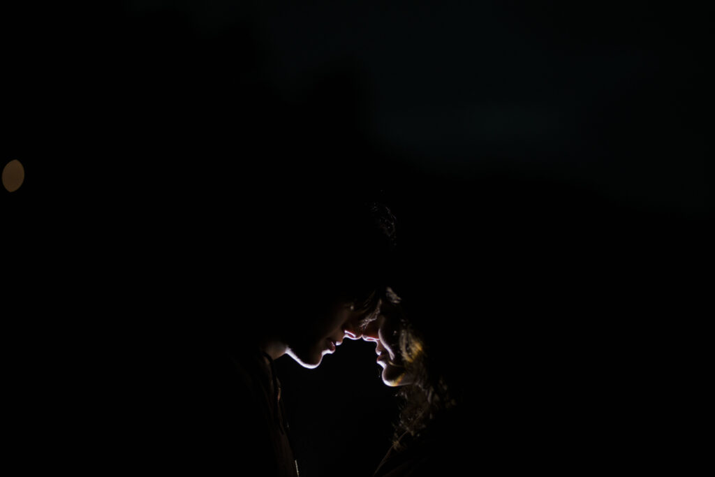 couple stand close face to face illuminated only by a flashlight during blue hour on the Oregon Coast