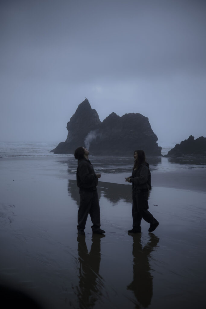 A couple smokes a shared cigarette in the misty blue hour on the Oregon coast