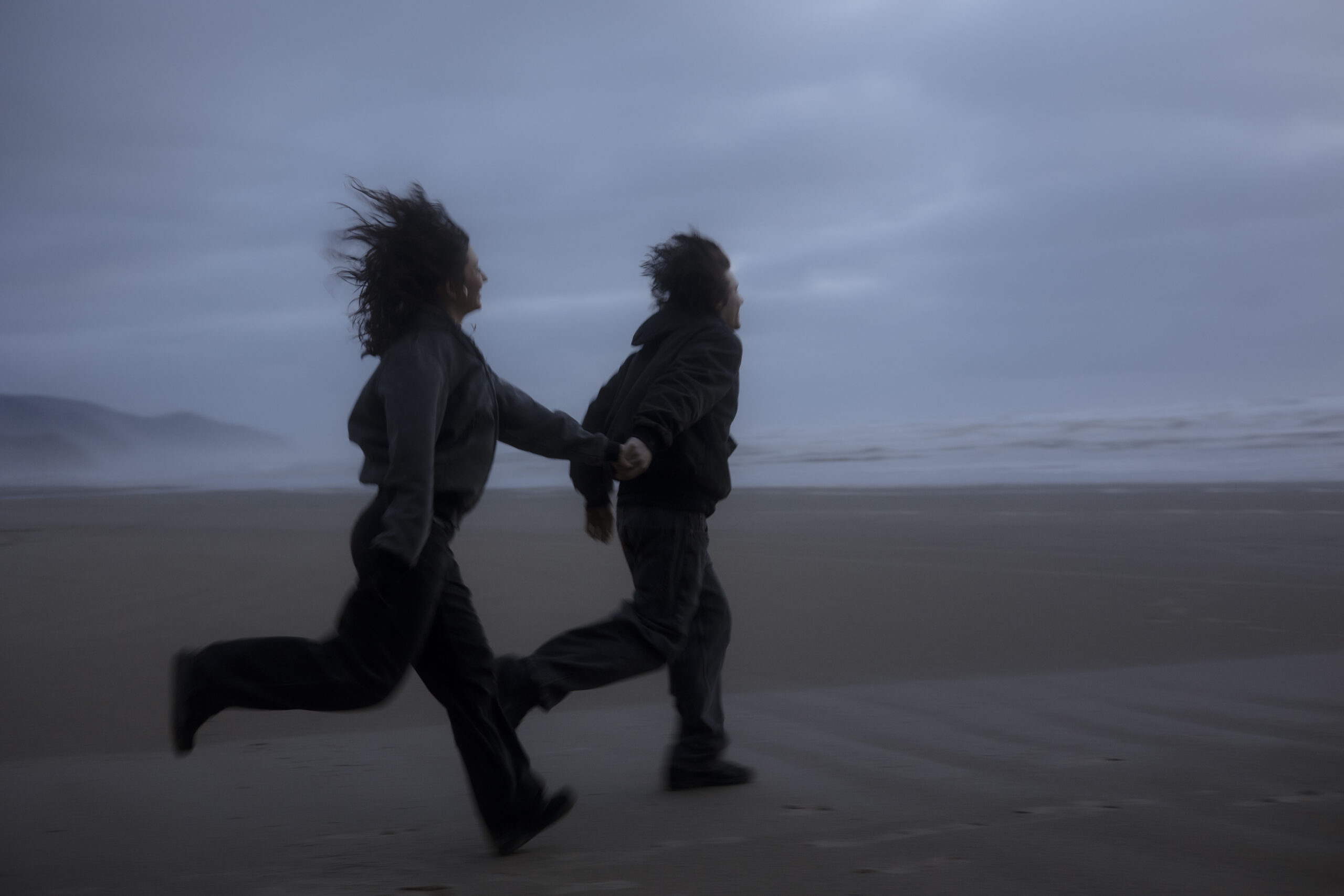 A couple runs hand in hand along the coastline in Oregon at blue hour