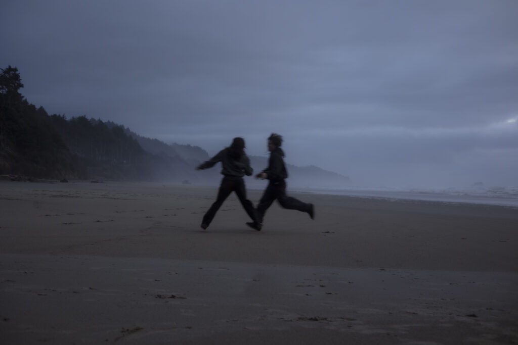A couple playfully runs together along the Oregon coastline during blue hour