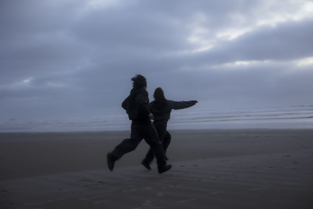 A couple runs along the beach during blue hour on the Oregon Coast