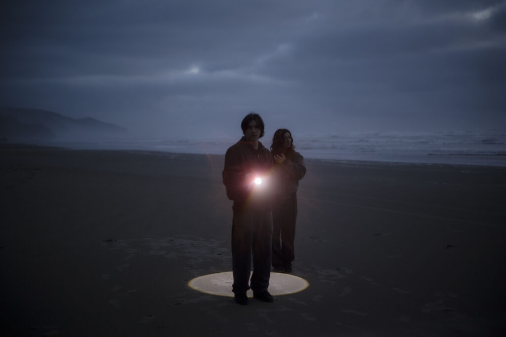 A couple explore the coastline with a flashlight during blue hour on the Oregon Coast