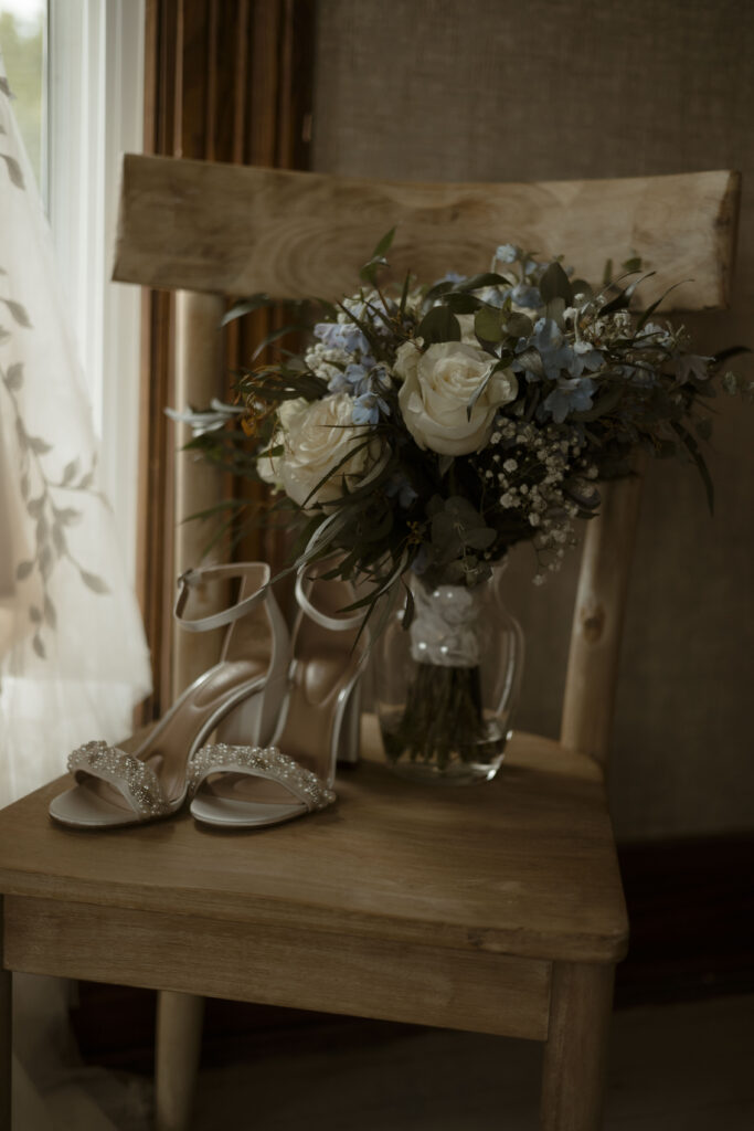 Callies bridal bouquet rests in a glass vase on a wooden chair next to her shoes