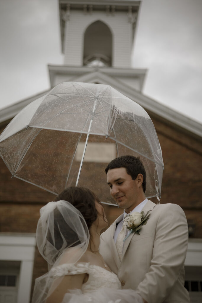 Callie and Matt cuddle together under an umbrella outside the church