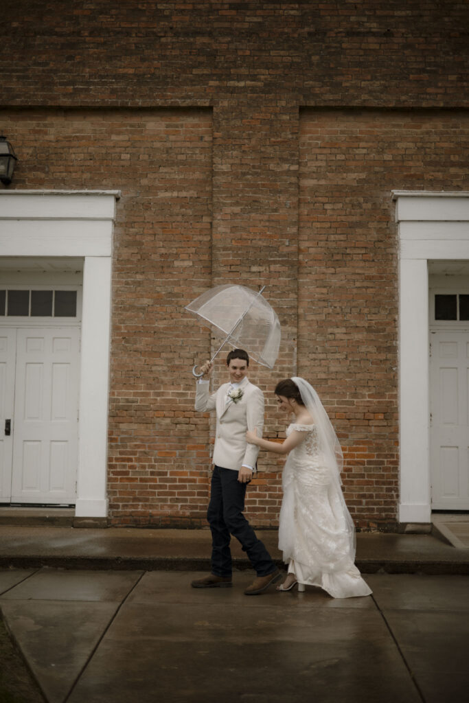 Callie and Matt walk in front of the church under the umbrella